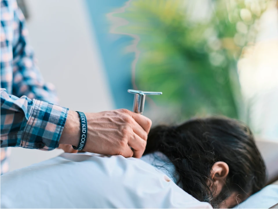Hands of a Chiropractor Using an Integrator to Adjust the Spine of a Patient